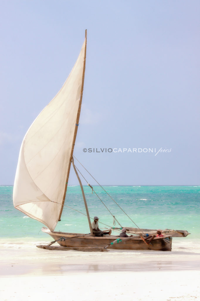 Waiting for the wind the fishermen are sitting on their boat lying on the shore, Zanzibar, Tanzania
