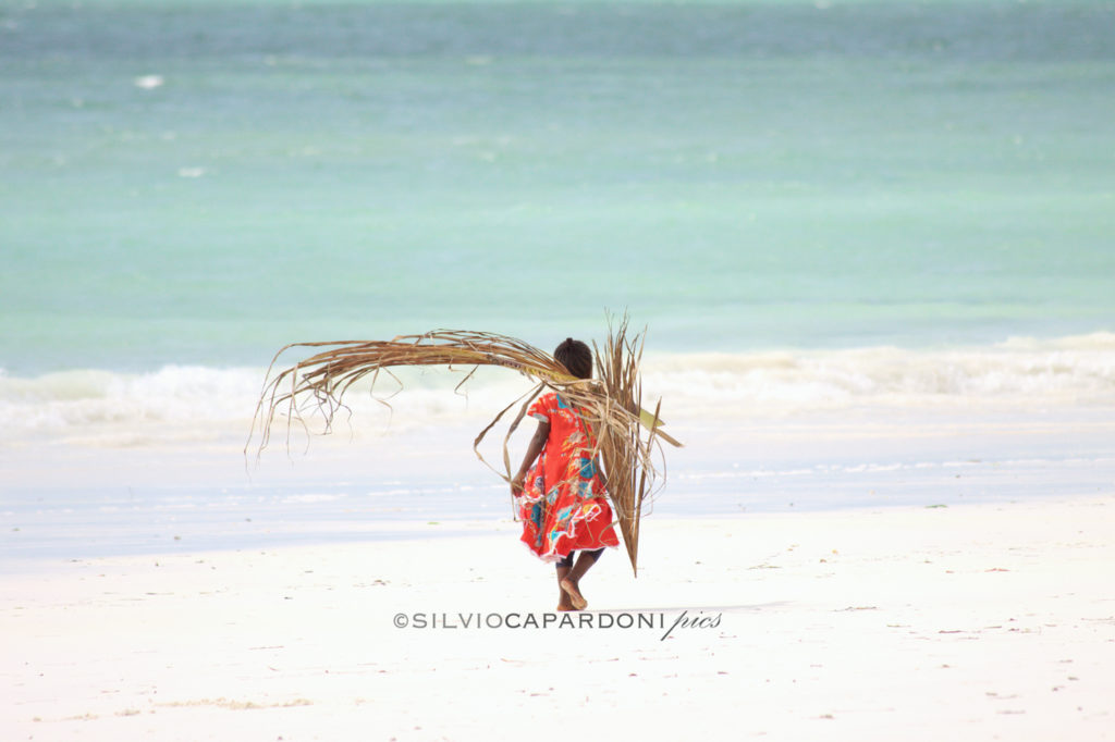 Little girl on the beach with palm leaves walking on the shoreline, Zanzibar, Tanzania